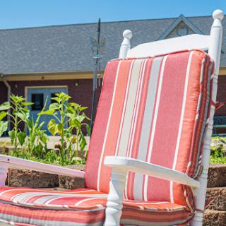 A cozy rocking chair with striped cushions, inviting relaxation in a sunlit garden.