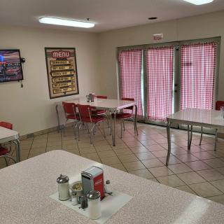 An empty diner with several tables and chairs arranged neatly, featuring pink curtains on the windows.