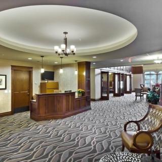 A spacious hotel lobby featuring a wooden reception desk, elegant chandelier, and comfortable seating.