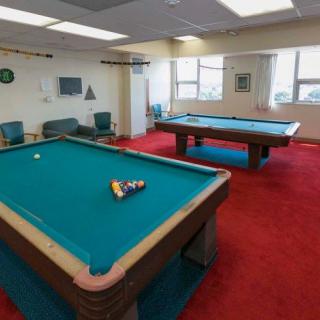 A recreation room featuring two pool tables with a red carpet flooring and large windows.