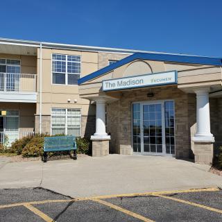 Entrance of a modern commercial building with large windows and a bench outside.