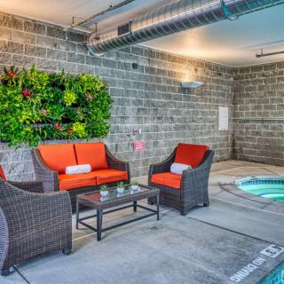 Indoor seating area with rattan chairs and a hot tub, featuring vibrant orange cushions and a vertical garden on the brick wall.