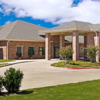A brick residential building with a covered entrance and landscaped driveway.