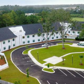 Aerial view of a white building with a parking lot surrounded by greenery.