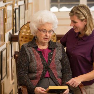 A caregiver comforting an elderly woman holding a book in a home setting.