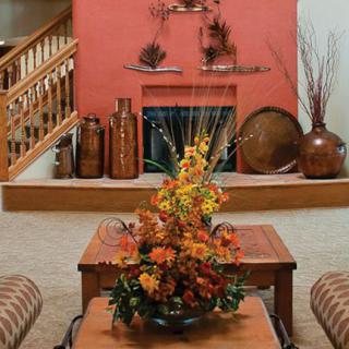 A cozy living room with autumn-themed decorations, featuring a fireplace and a floral centerpiece on wooden tables.