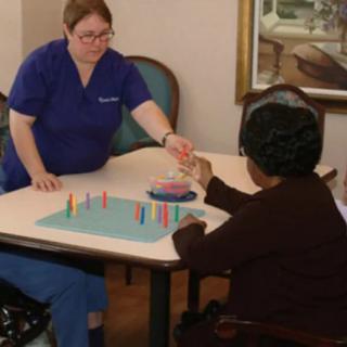 A healthcare worker assists an elderly person with a therapeutic activity.