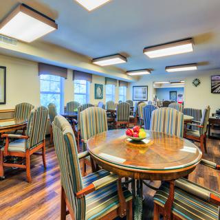 A spacious dining room with multiple tables and chairs, featuring a wooden floor and bright lighting.