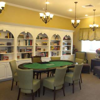 A cozy room featuring a poker table surrounded by chairs, with built-in bookshelves in the background.