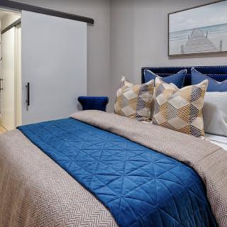 A modern bedroom with a neatly made bed featuring a blue blanket and patterned pillows, complemented by wall art.