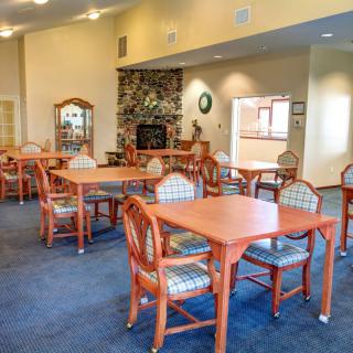 A well-furnished dining room with several wooden tables and chairs, decorated with a carpeted floor and warm lighting.