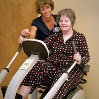 A caregiver assisting an elderly woman on a fitness machine, promoting health and rehabilitation.