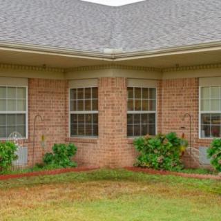 A brick house corner with multiple windows and well-maintained shrubs in front.