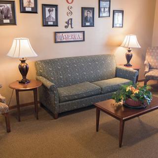 A cozy living room with a sofa, two lamps on side tables, and a coffee table with a floral centerpiece. The walls are decorated with framed pictures.
