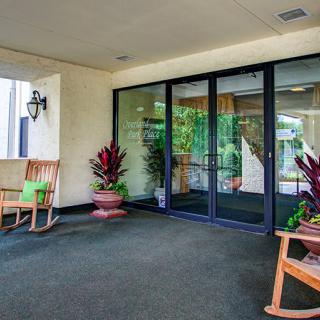 A welcoming entrance area with glass doors, rocking chairs, and potted plants.