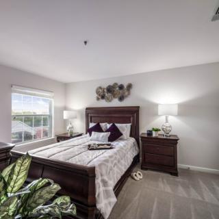 A well-lit bedroom with a neatly made bed, wooden nightstands, and decorative elements.
