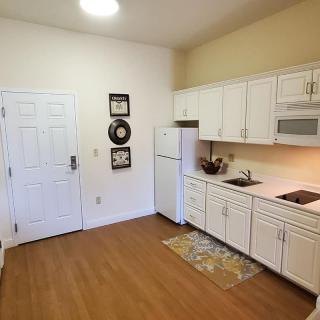 A modern kitchen interior with white cabinets, a fridge, and a microwave on a hardwood floor.