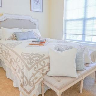 A cozy bedroom with a neatly made bed, decorative pillows, and a bench by the window.