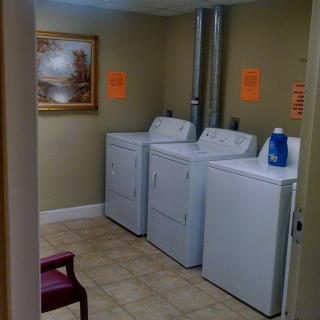 A small laundry room with washing machines and dryers, featuring a bottle of detergent.
