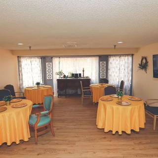 A well-arranged dining area with tables covered in yellow tablecloths and matching chairs, set against a softly lit interior.