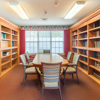 A quiet library room with a large table and surrounding bookshelves, ideal for meetings or study sessions.