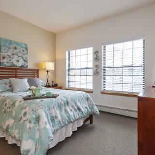 A well-lit bedroom with a cozy bed, floral bedding, and decorative artwork on the wall.