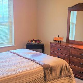 A cozy bedroom with a neatly made bed, wooden dresser, and a mirror by the window.