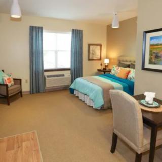 A cozy bedroom with a neatly made bed, chair, and table by the window.