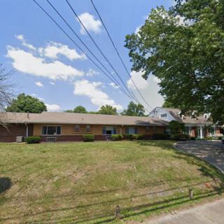 A suburban brick house with a large lawn and driveway under a clear blue sky.