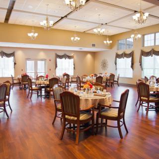 A spacious and elegant dining area with neatly arranged tables and chairs, featuring warm lighting.
