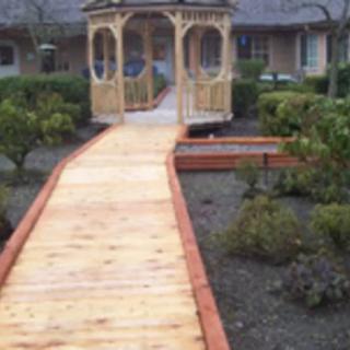 A picturesque wooden walkway leading to a charming gazebo surrounded by garden greenery.