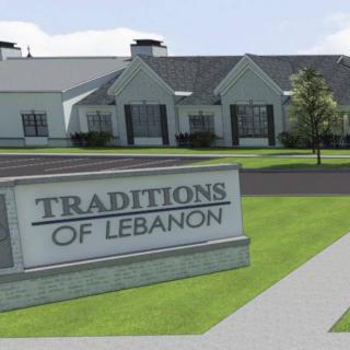 A sign reading 'Traditions of Lebanon' in front of a building with a well-maintained lawn.