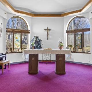 A serene chapel with an altar, featuring a cross on the wall and large windows overlooking a natural view.
