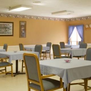 An empty dining room with tables and chairs neatly arranged, featuring tablecloths and a window with curtains.