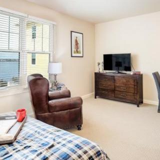 A cozy bedroom with a comfortable chair, TV on a dresser, and large window.