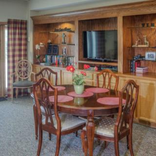 A cozy dining area with a round wooden table, surrounded by chairs and a built-in entertainment center featuring a television and shelves.