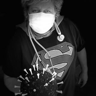 Person wearing a superhero t-shirt and mask, holding a model of a virus with syringes in it.