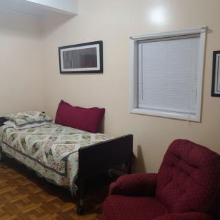 A simple bedroom with a single bed, burgundy armchair, and framed pictures on the wall.