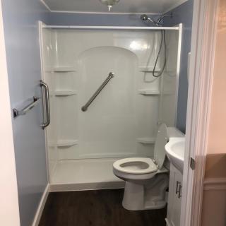 A compact, accessible bathroom featuring a shower with grab bars, a toilet, and a small sink.