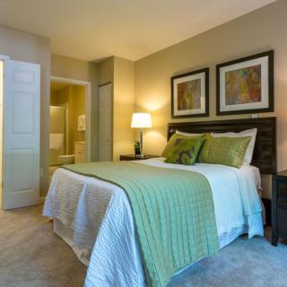 A cozy and modern bedroom featuring a neatly made bed with green accents, bedside lamp, and framed artwork on the walls.