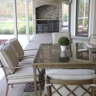 A cozy screened patio with cushioned seating and a glass table, complete with an outdoor fireplace.
