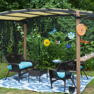 A cozy outdoor patio setup with chairs and a table under a canopy, surrounded by garden decorations.