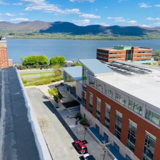 A scenic view of a modern building along the river, framed by mountains under a clear blue sky.
