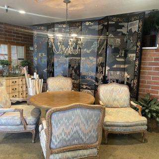 A cozy interior space featuring a round table with upholstered chairs, set against a decorative screen and brick wall, with plants adding a touch of greenery.