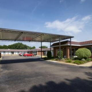 A motel exterior with a parking lot and a covered entrance on a sunny day.