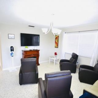 A modern living room with comfortable chairs arranged around a television and fireplace, illuminated by bright lighting.