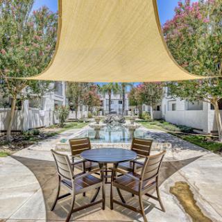 A serene outdoor patio area with a stylish shade sail, offering a perfect spot for relaxation near a beautiful water feature.