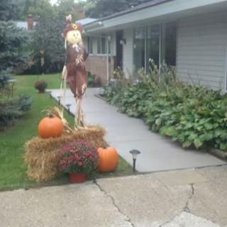 A front yard decorated with pumpkins, a scarecrow, and a hay bale for autumn.