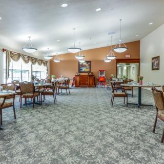 A spacious dining area with multiple tables and chairs, featuring elegant lighting and carpeted floors.