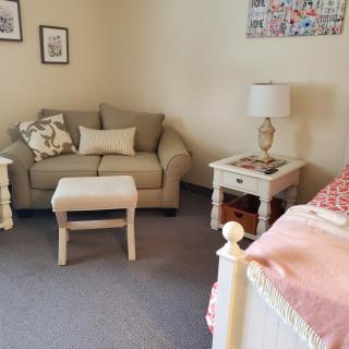A cozy living room with a sofa, side table, lamp, and bed.